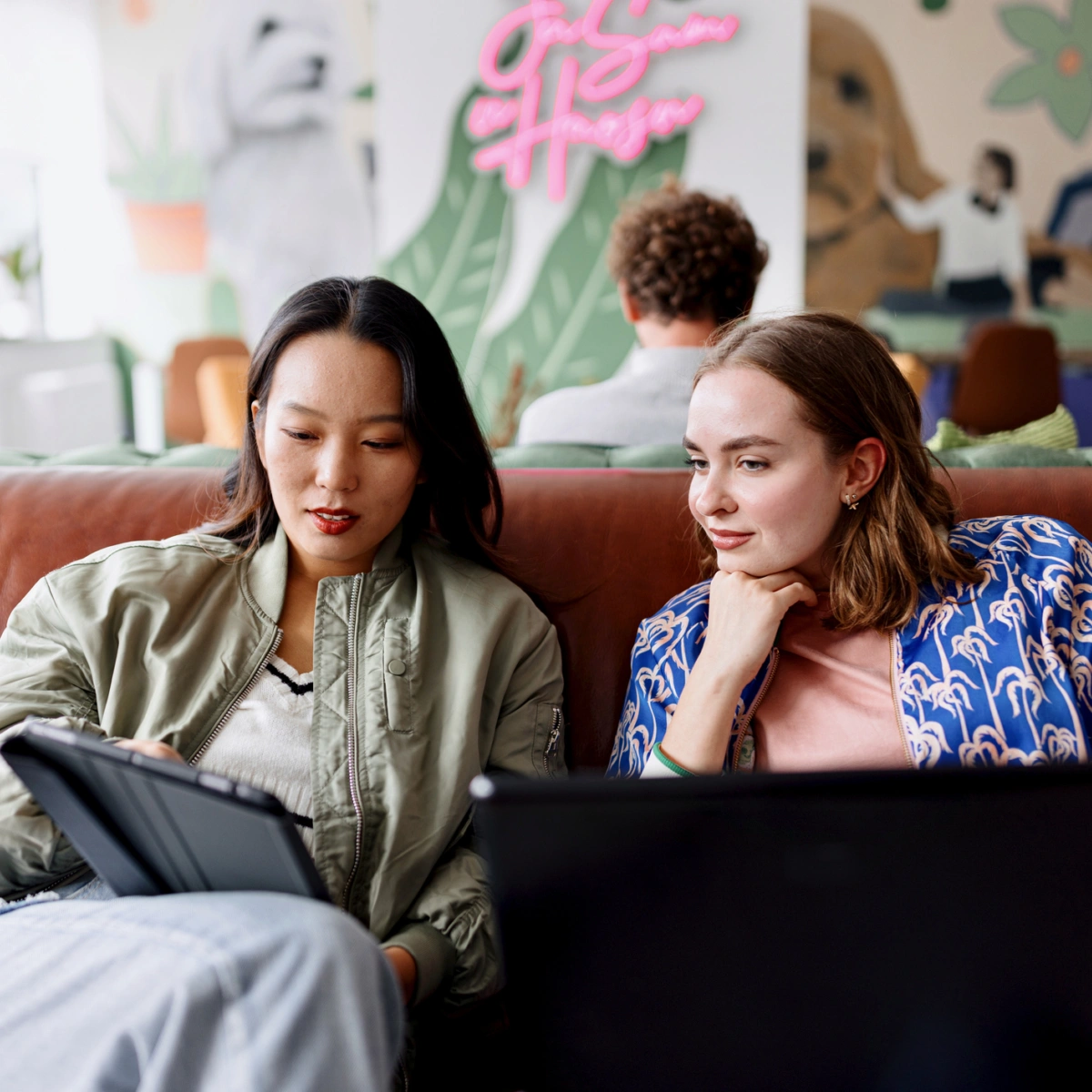 To kollegaer samarbeider med nettbrett og laptop i et uformelt kontormiljø